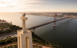 LISBON, PORTUGAL - CIRCA AUGUST, 2021: Aerial scenery of long suspension bridge over calm river in evening in Lisbon