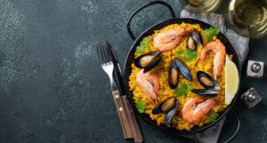 Traditional spanish seafood paella in pan with chickpeas, shrimps, mussels, squid on black concrete background. Top view with copy space.