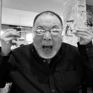 Ασπρόμαυρη φωτογραφία του Ai Weiwei, που καλύπτει τα μάτια του με δύο κουτάλια