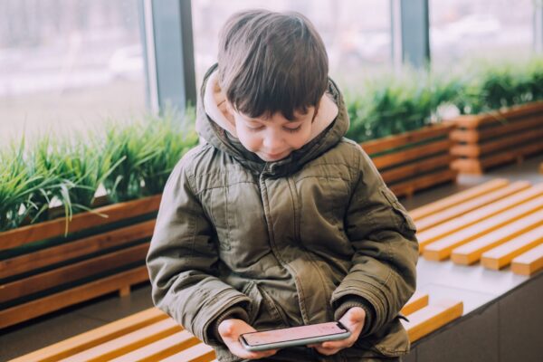 Ένα παιδί κάθεται σε ένα παγκάκι και διαβάζει στο κινητό