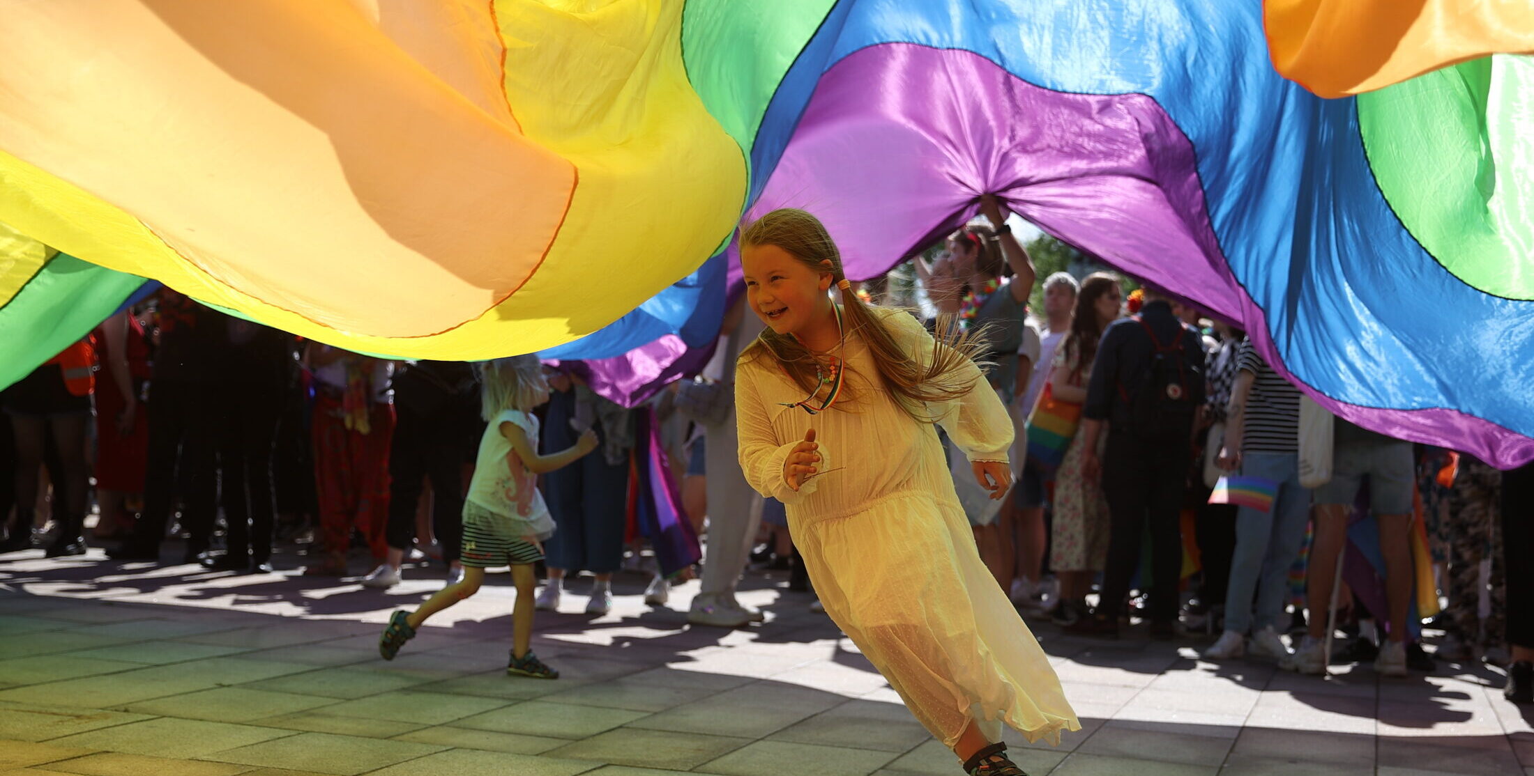 Κοριτσάκι τρέχει χαρούμενο κάτω από τη σημαία pride lgbtq+