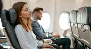 γυναίκα και άνδρας κάθονται μέσα σε αεροπλάνο με ανακλινόμενα καθίσματα