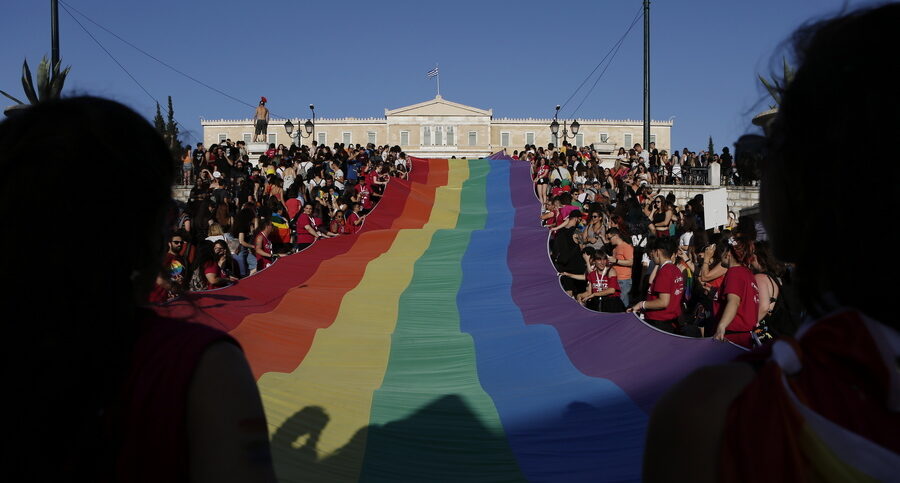 Άνθρωποι κρατούν μια γιγαντιαία σημαία του ουράνιου τόξου μπροστά από το κοινοβούλιο, καθώς συμμετέχουν στο Athens Pride