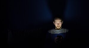Φωτογραφία ενός ατόμου σε σκοτεινό φόντο που κοιτάει το κινητό του